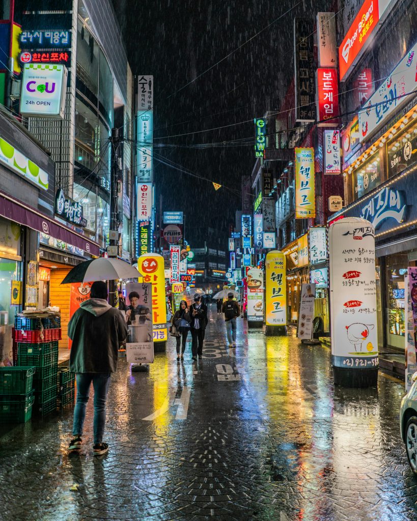 Colorful neon-lit street in Seoul, South Korea showing bustling nightlife with reflections on wet pavement.